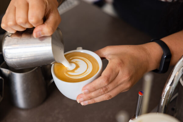 Pouring steamed milk to create latte art into mug